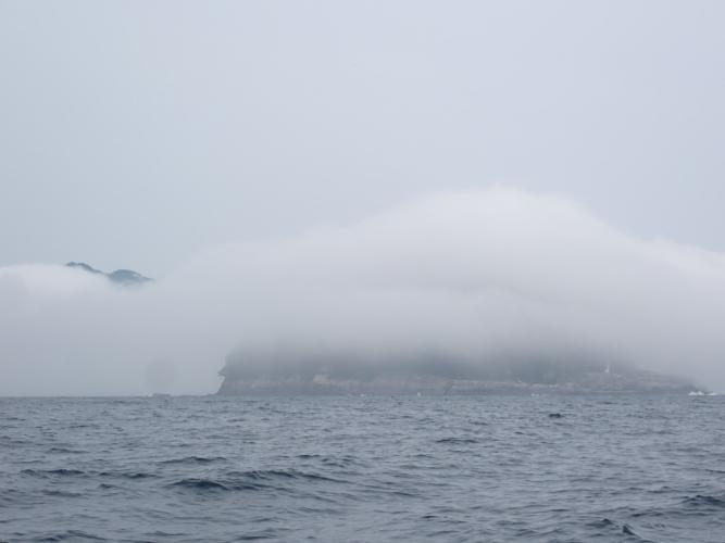 Into and out of the fog. Lighthouse on RHS of island indicates scale.