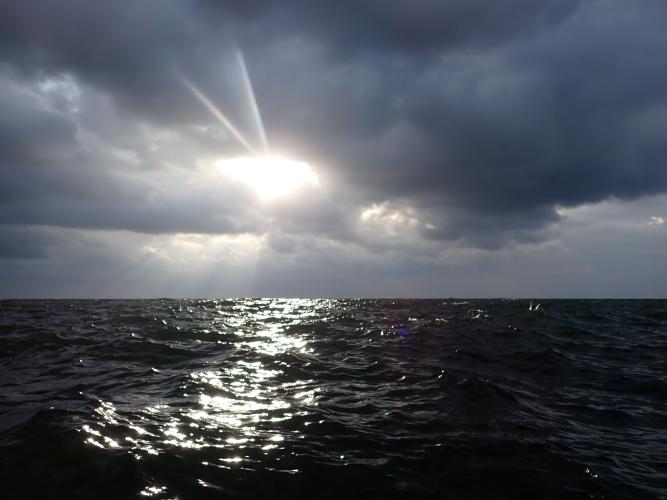 The sun pokes through on a choppy and windless sea